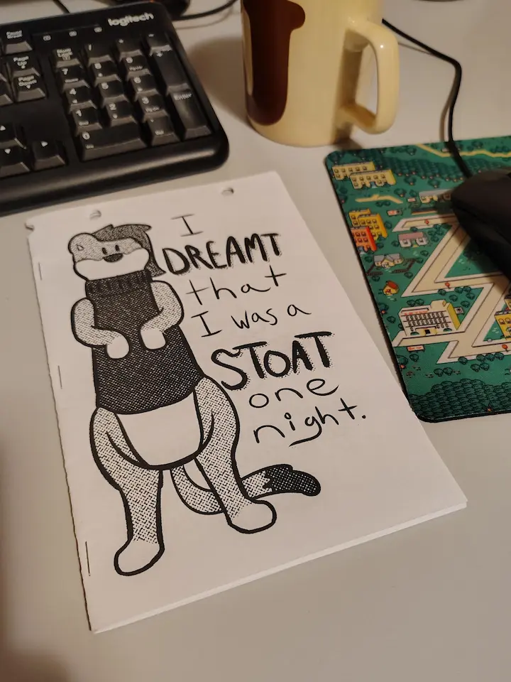 Photo of the first printed copy of my zine 'I Dreamt I Was a Stoat One Night,' sitting on my desk. It's a little shoddy, printed on holed paper, stapled wrong... and it's all mine! ❤️
